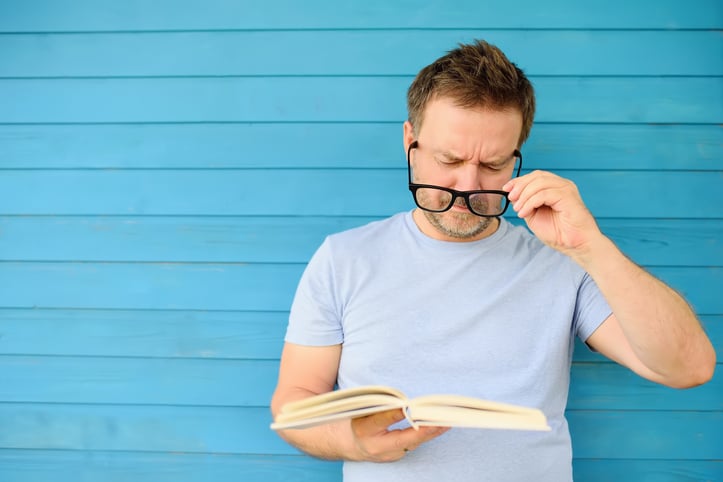 mature man with big black eye glasses trying to read book
