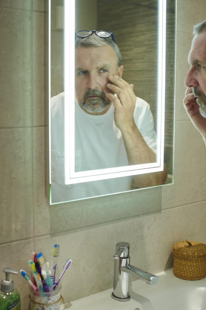 A mature man inspecting his eye in the bathroom