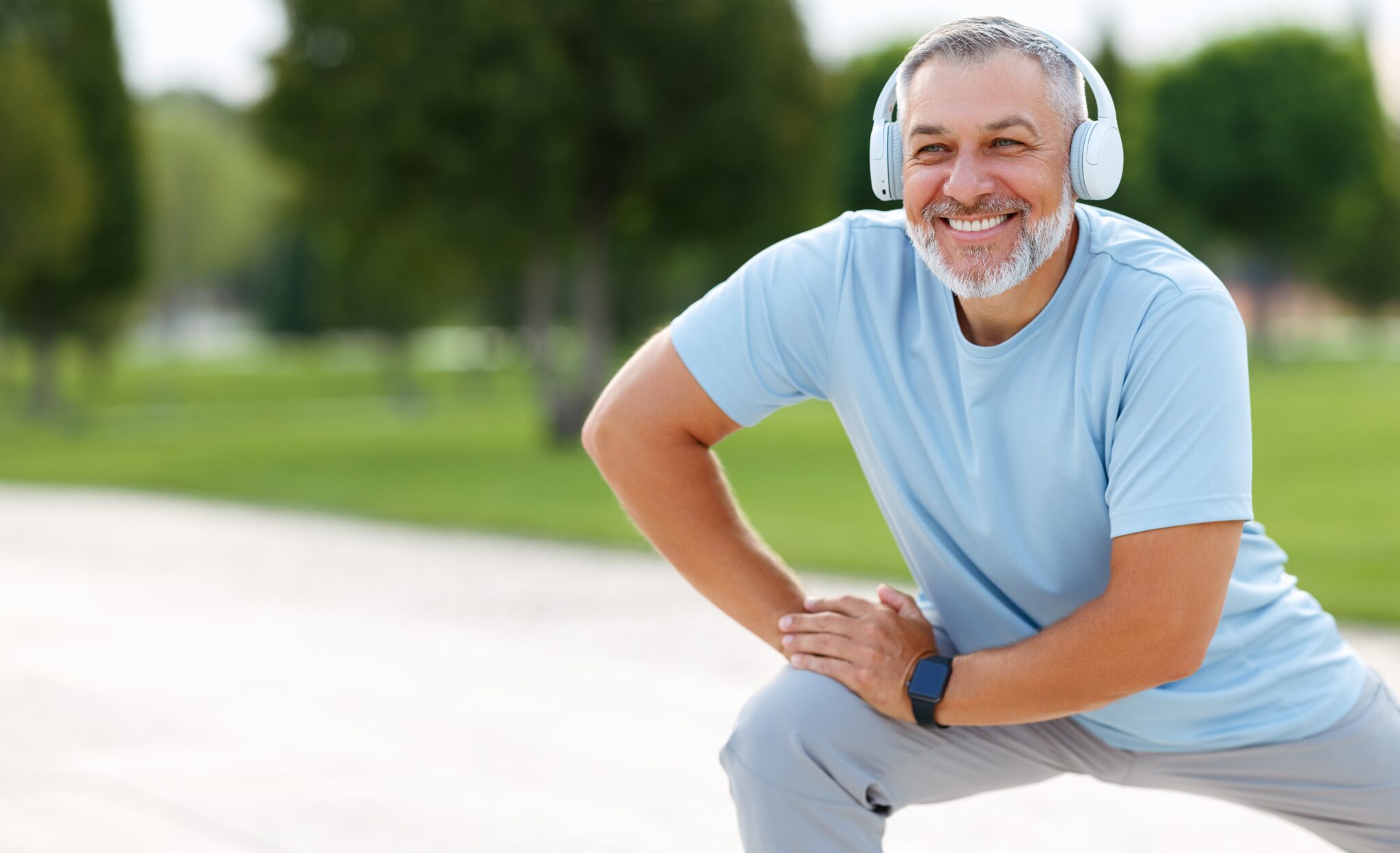 Senior man wearing headphones and sports outfit warming up muscles